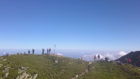 hikers stand on a mountain peak looking out across the landscape with amazing blue sky and low clouds in the valley below