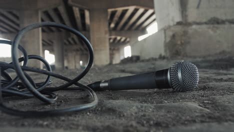 Close-up of a microphone with cable lying on the ground beneath a concrete bridge, evoking raw underground hip-hop and street rap culture