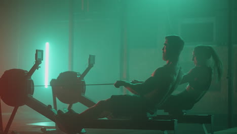 un hombre y una mujer realizan atletas fuertes realizan ejercicios en el gimnasio en una máquina de remo en cámara lenta