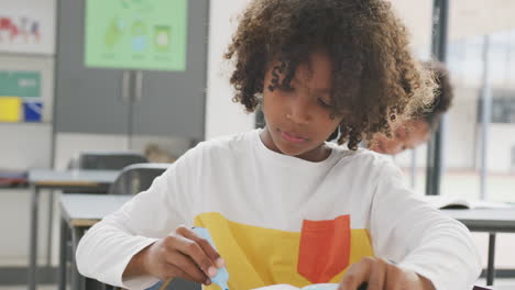 Video-portrait-of-smiling-african-american-schoolboy-working-at-desk-in-class