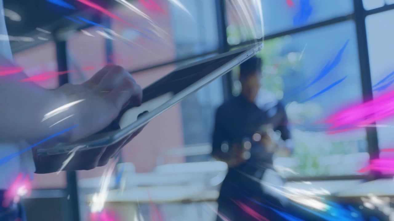 Hånd som holder nettbrett strømmer data på et moderne kontor, som viser en uskarp kollega som holder smarttelefon