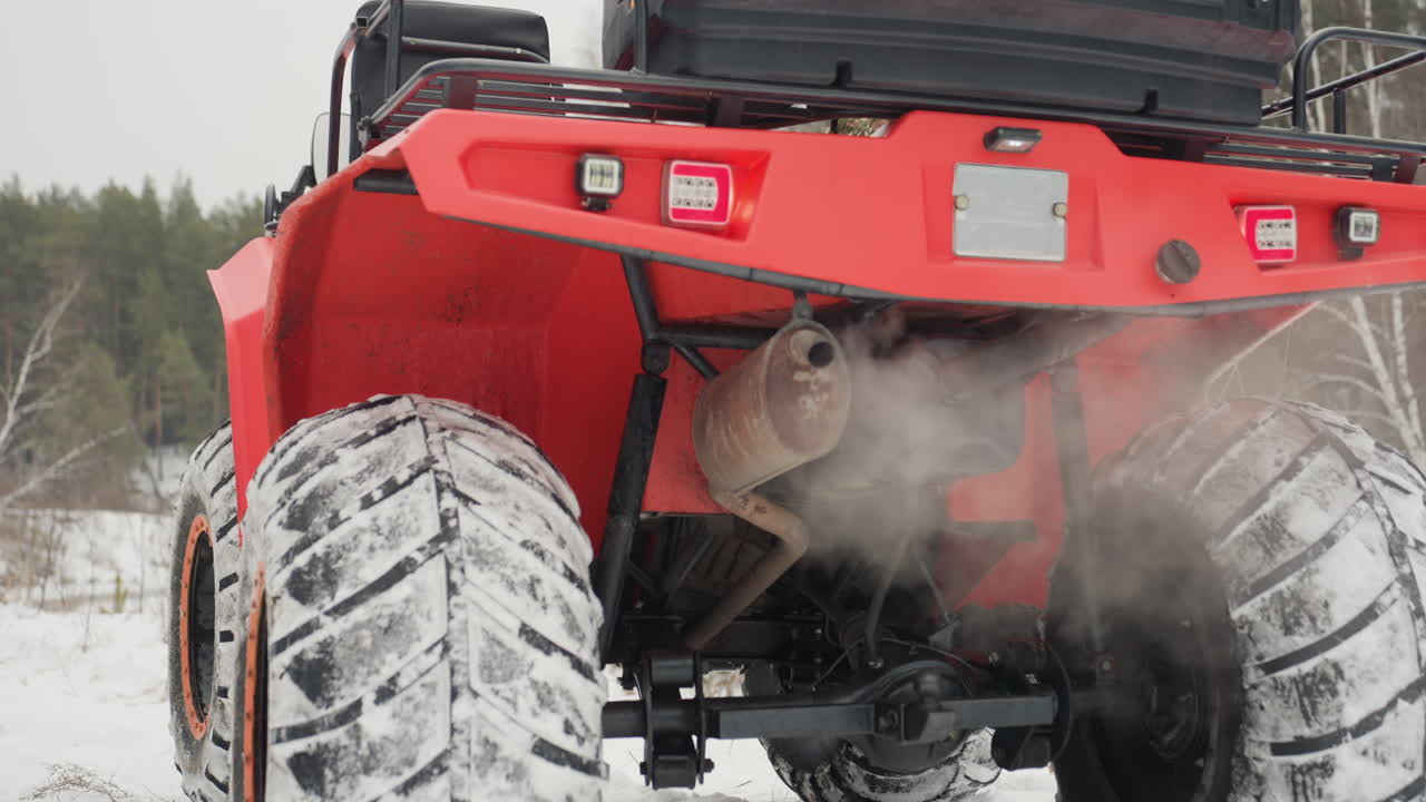 ATV rosso in una foresta innevata, vista posteriore che mostra lo scarico fumante e pneumatici con battistrada robusto che aderiscono al sentiero ghiacciato. Terreno invernale impervio, cielo coperto, atmosfera di natura selvaggia isolata, estremo carico di adrenalina.