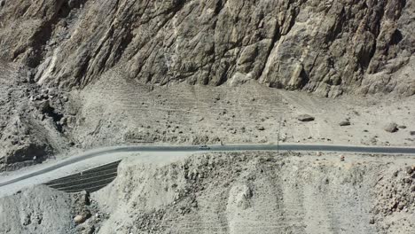 Luftdrohne-Verfolgt-An-Einem-Sonnigen-Sommertag-Ein-Lokales-Weißes-Auto-Auf-Der-Unbefestigten-Autobahn-In-Den-Schroffen-Bergen-Von-Skardu,-Pakistan-Entlang-Des-Indus-Flusstals