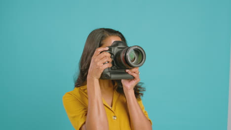 mature female photographer with camera against blue background on shoot in studio