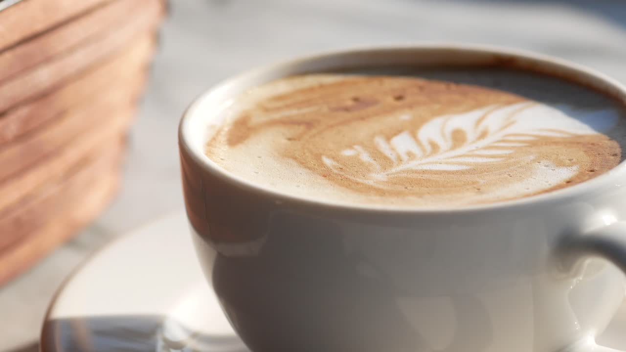A close-up of a white coffee cup with intricate leaf-shaped latte art