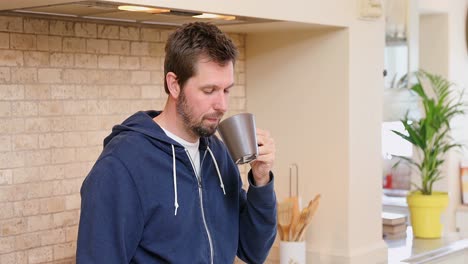 Young-man-leaning-on-kitchen-counter-having-coffee-4K-4k