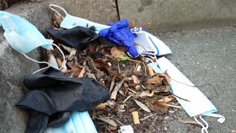 Dirty-disposable-corona-virus-face-masks-and-latex-gloves-among-cigarette-junk-litter-on-street-curb-descending-dolly-left