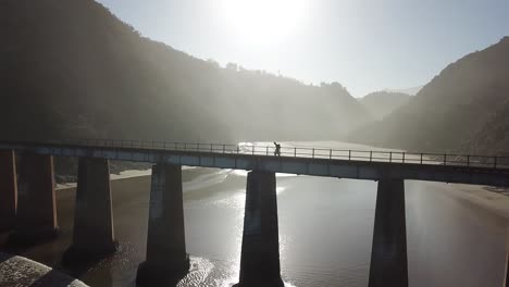 drone video of man walking accross a giant bridge at sunset