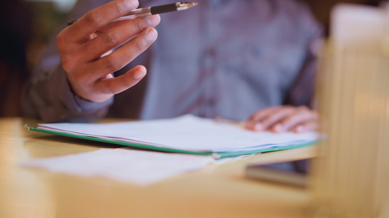 Young man in formal shirt drawing on white paper with black pen at wooden table, focused on precise lines, both hands visible, suggesting creativity, concentration, design process