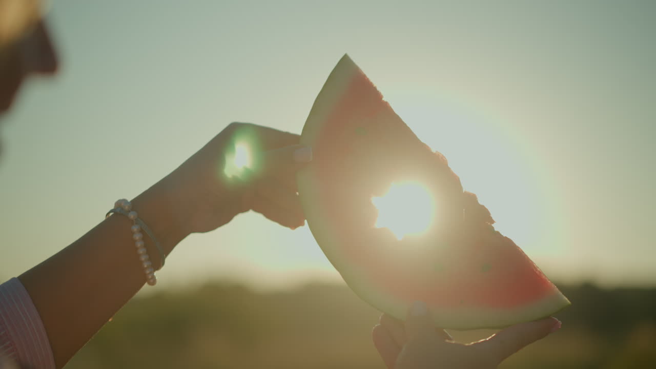 빛이 빛나면서 아름다운 빛 효과와 반이는 실루을 만드는 별의 절단 모양의 수박 조각을 들고 있는 여성의 클로즈업