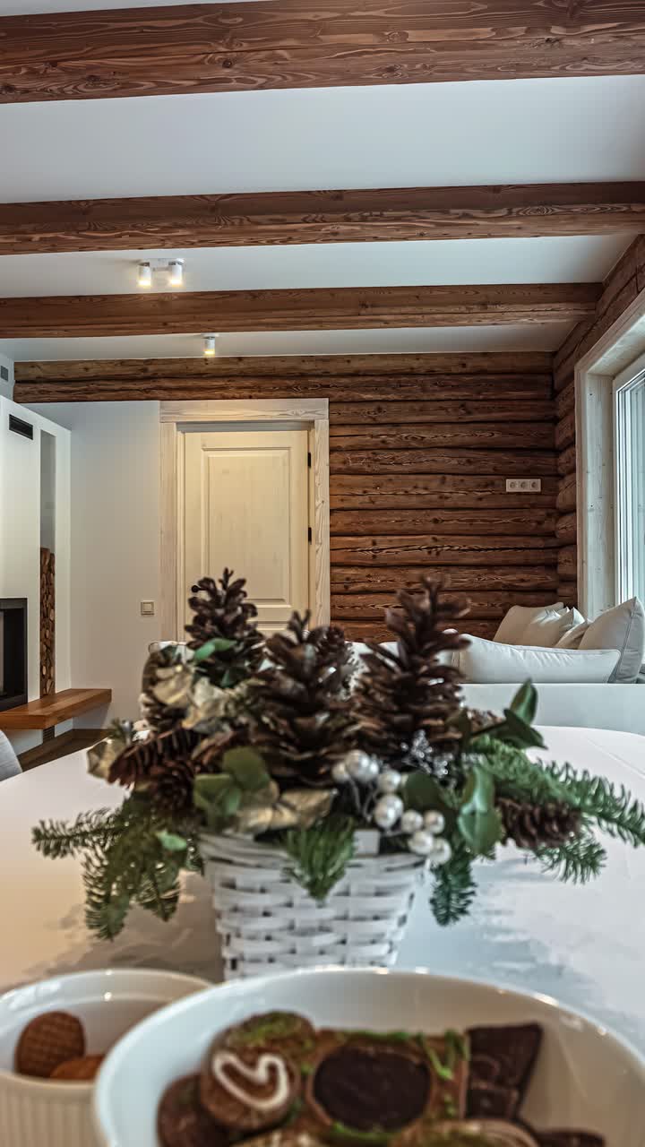 A vertical revealing shot showcases the beautiful interior design of a modern rustic log cabin in Latvia, featuring exposed wooden beams, a cozy fireplace, and a table with Christmas decorations