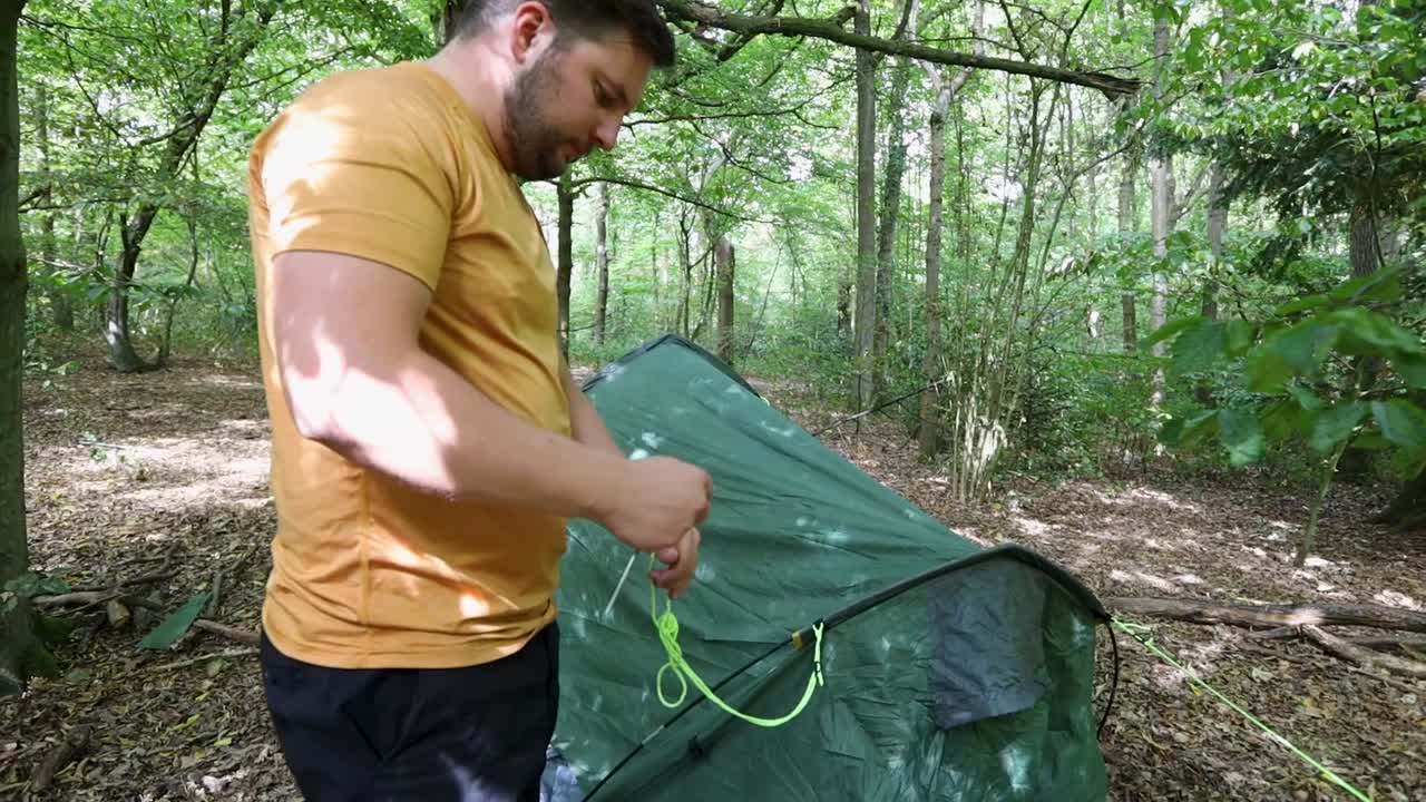 Young man untangling string of tent in the forest camping zone, handheld view
