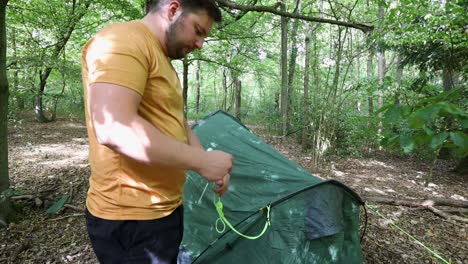 young man untangling string of tent in the forest camping zone, handheld view