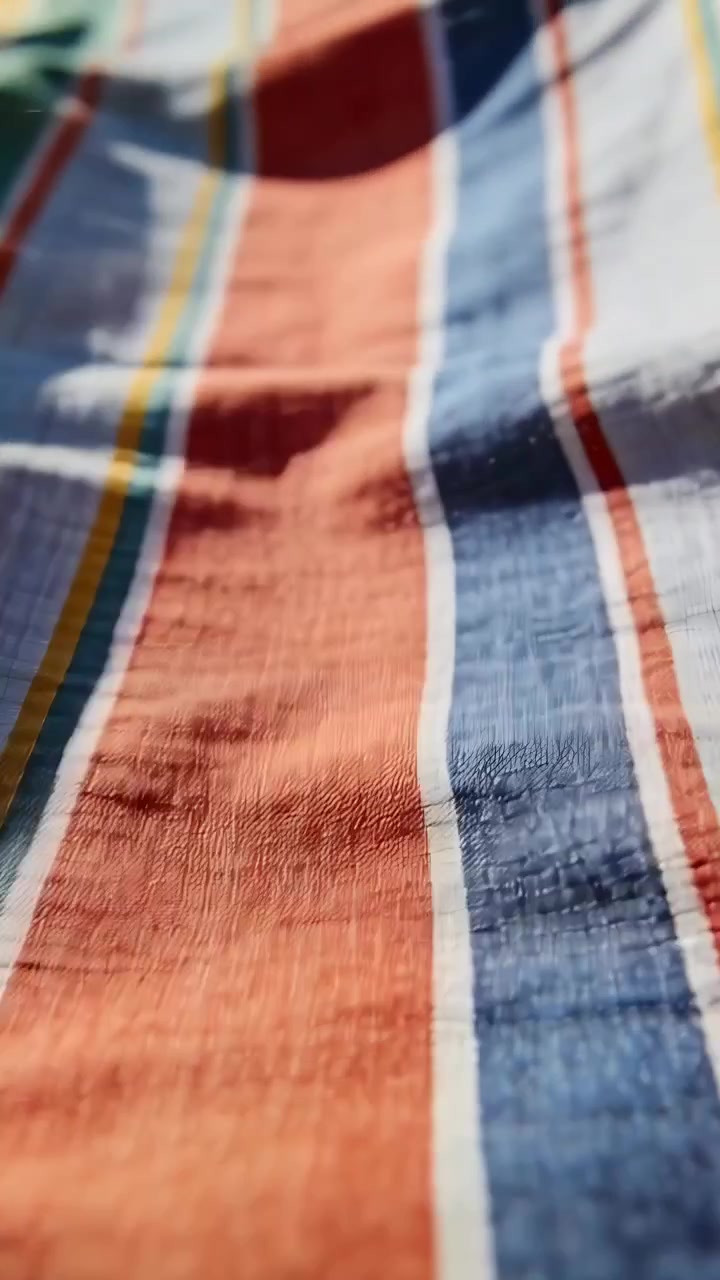 Vertical video: Pulling back camera revealing woven striped cloth on flat surface, showing texture