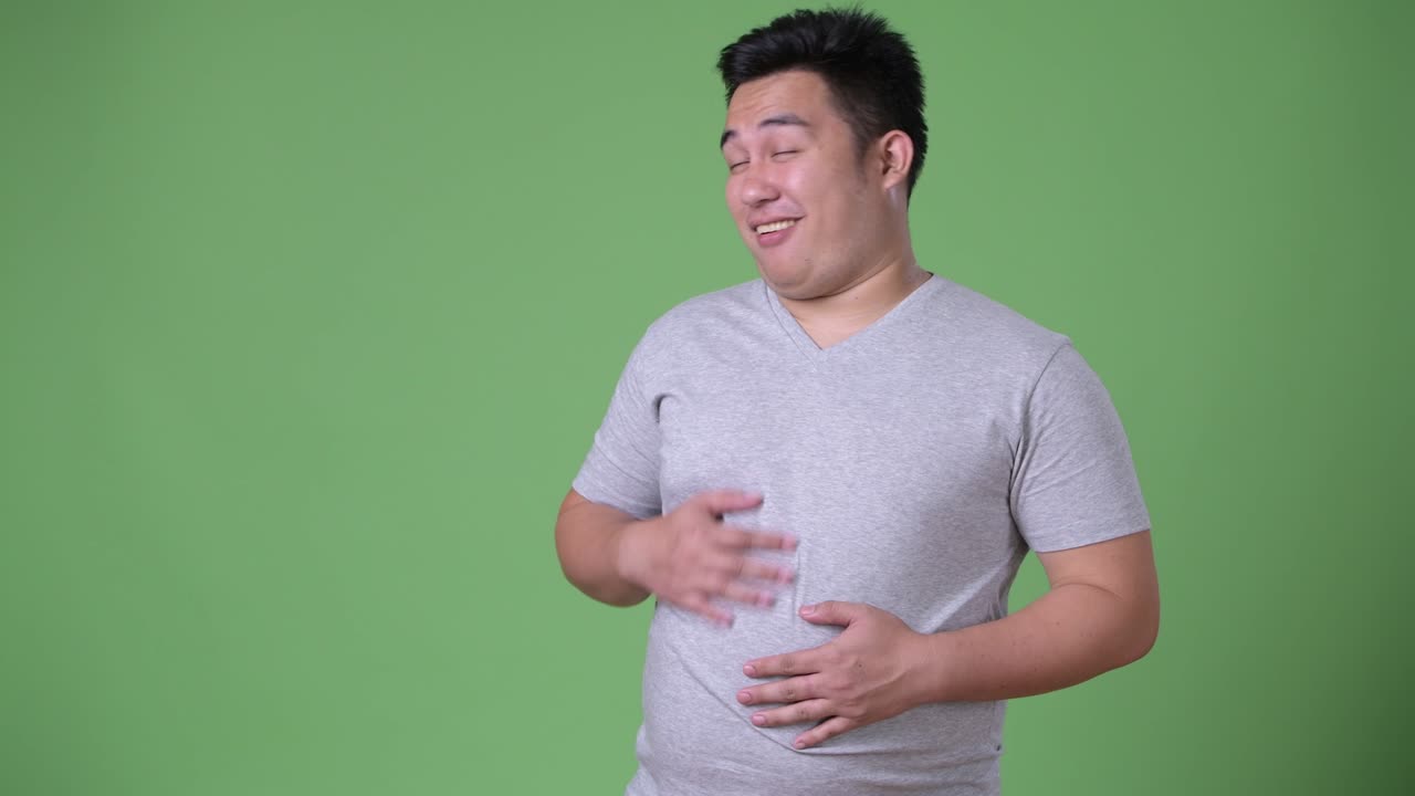 Young handsome overweight Asian man against green background
