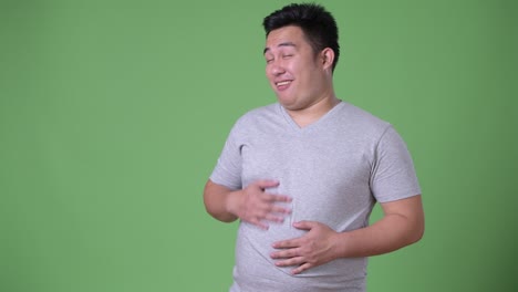 young handsome overweight asian man against green background