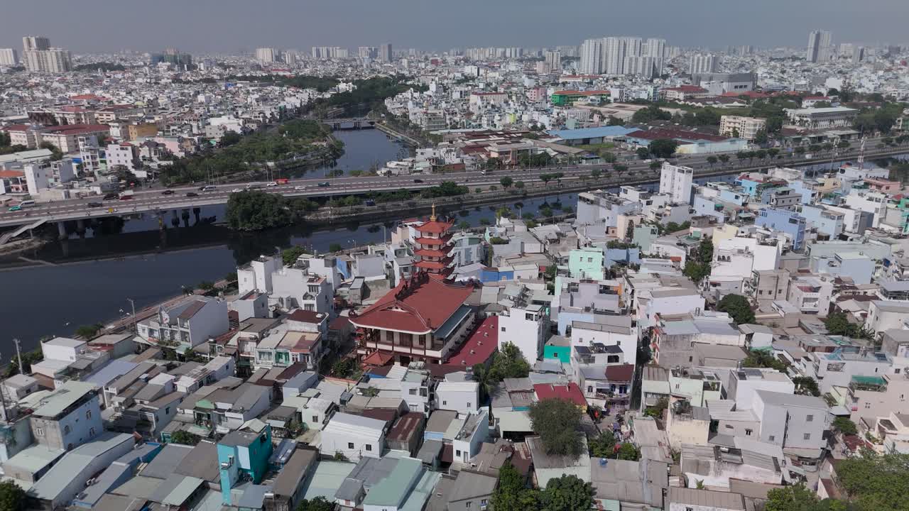 Fly in establishing drone view over Buddhist pagoda in busy urban area of Ho Chi Minh City, Vietnam on a sunny clear day featuring transportation infrastructure of maain roads and canals
