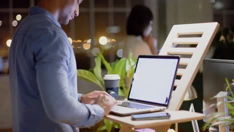 Biracial-casual-businessman-using-laptop-with-copy-space-at-standing-desk-at-night,-slow-motion