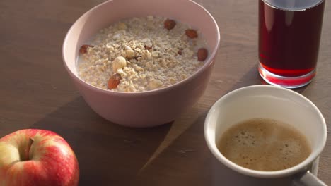 a breakfast table in the morning, consisting of a glass of juice, a bowl of muesli, a cup of coffee and an apple, close shot slow motion