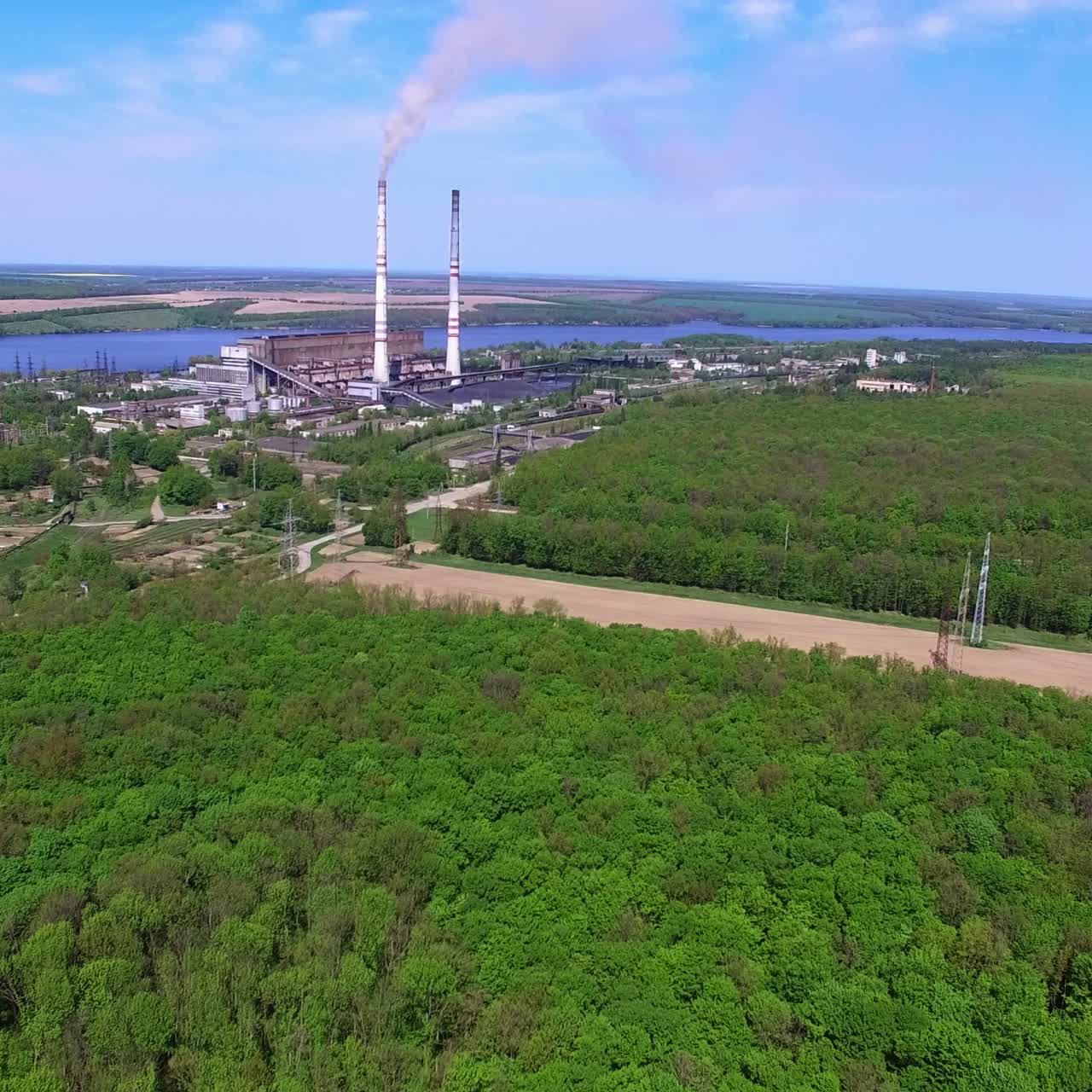 Sorvolo di una rigogliosa foresta verde vicino a una zona industriale. Stretto fiume e campi agricoli sullo sfondo
