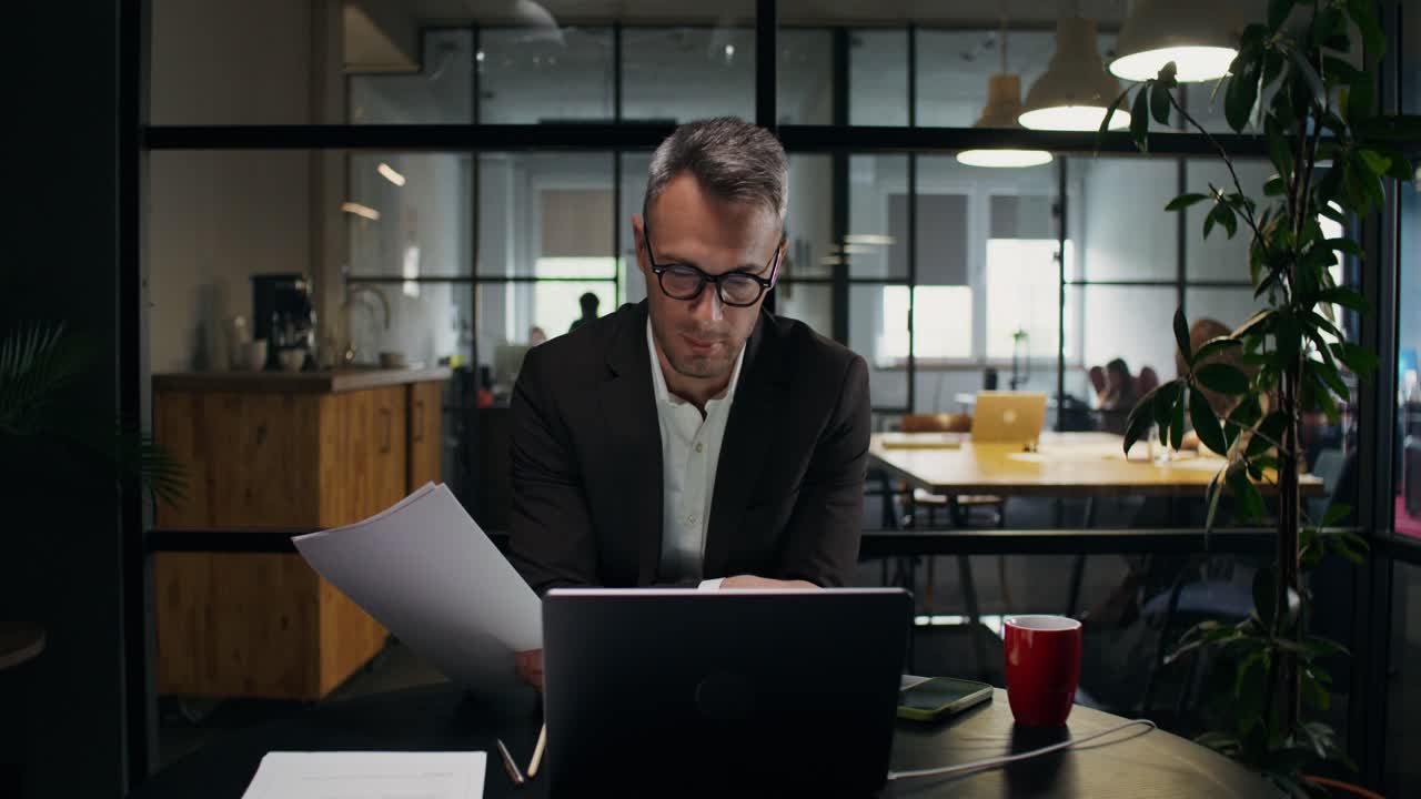 Uomo d'affari che esamina documenti sul portatile in un ufficio moderno