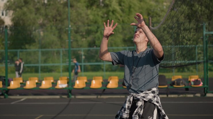 Back view of man playing volleyball as lady slams ball over net, with people in background on court, action-packed scene of volleyball game with athleticism, focus, and teamwork in bright sunlight