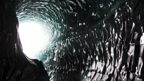 glass pattern on ice cave wall in iceland with bright light at end of tunnel