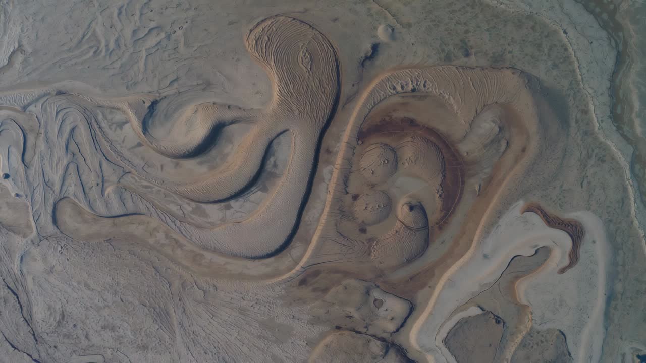 Hovering drone documenting curving sand ridges over tidal flat, drifting to reveal crescent ridge