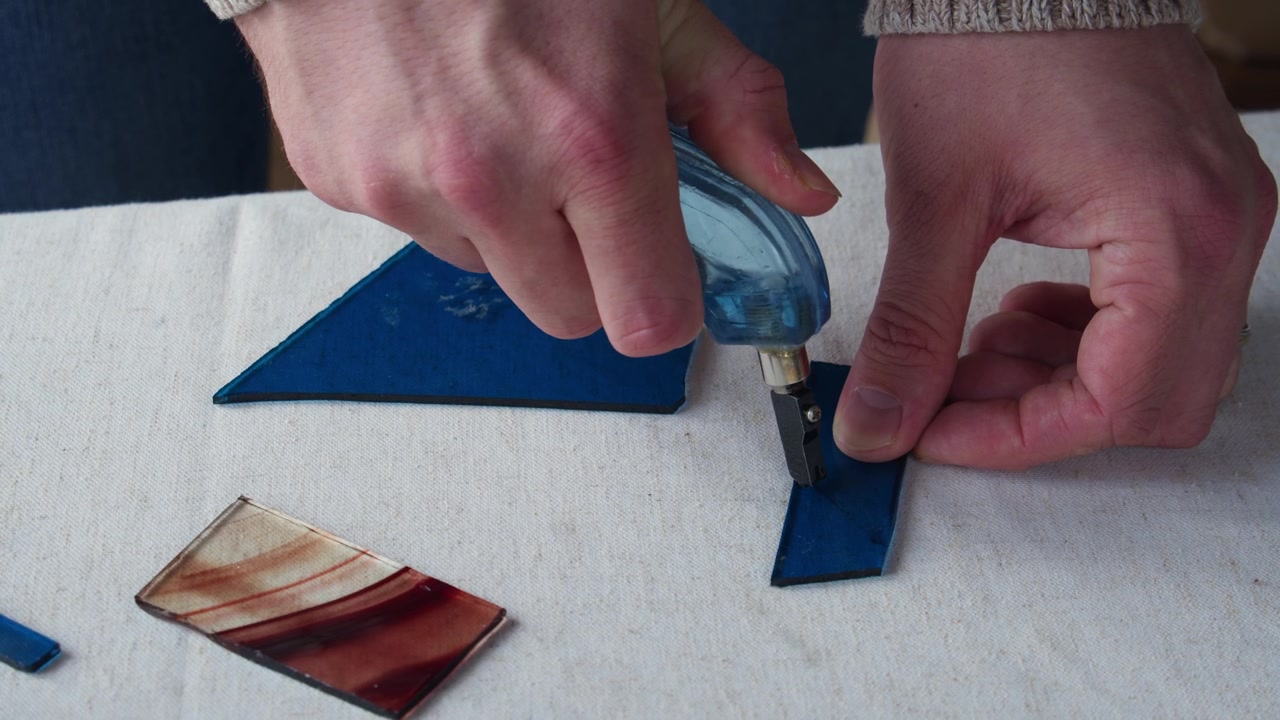 A small piece of dark blue glass is scored during an art class before being cut as a part of a larger stained glass design.