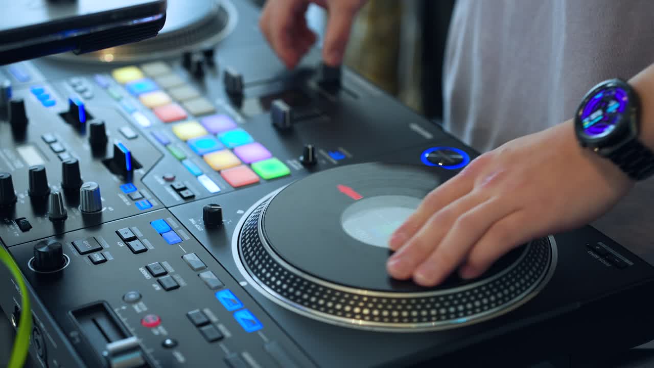Stüdyo veya kulüp ortamında renkli RGB pedleri, fader'ları ve düğmeleri olan profesyonel pikap kontrol cihazında plak çizen DJ ellerinin yakın çekimi.
