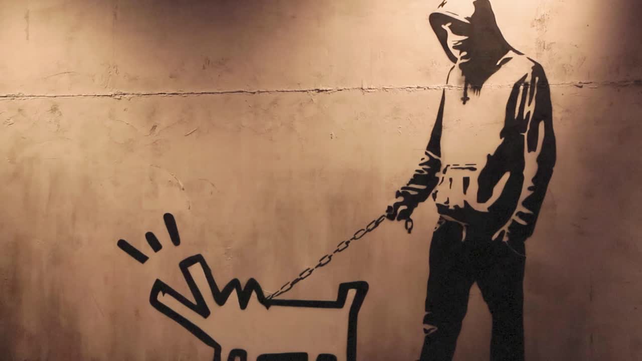 Wall stencil art of a man with a pixelated or 2d dog barking made by Banksy at his exhibition that is well lit.