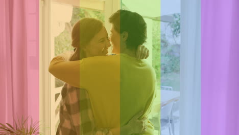 animation of pride rainbow stripes over happy caucasian lesbian couple embracing at home