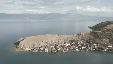 droneshot from above lin albania flying backwards on a cloudy day with the sun coming through the clouds with land and water underneath log