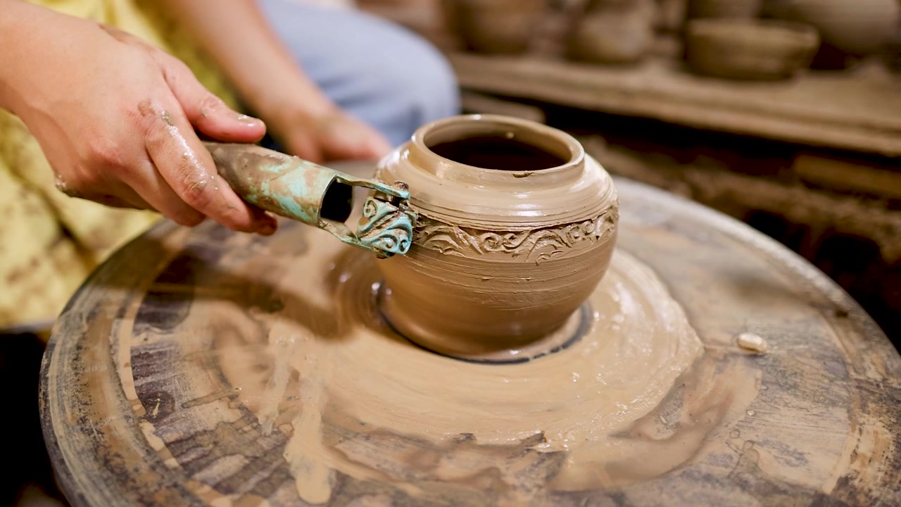 Primo piano di un vasaio che usa uno strumento metallico per intagliare disegni tradizionali su un vaso di argilla rotante