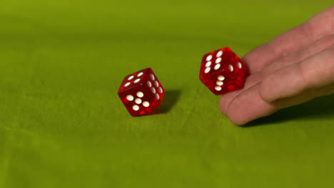 mano lanzando dos dados rojos en la mesa verde