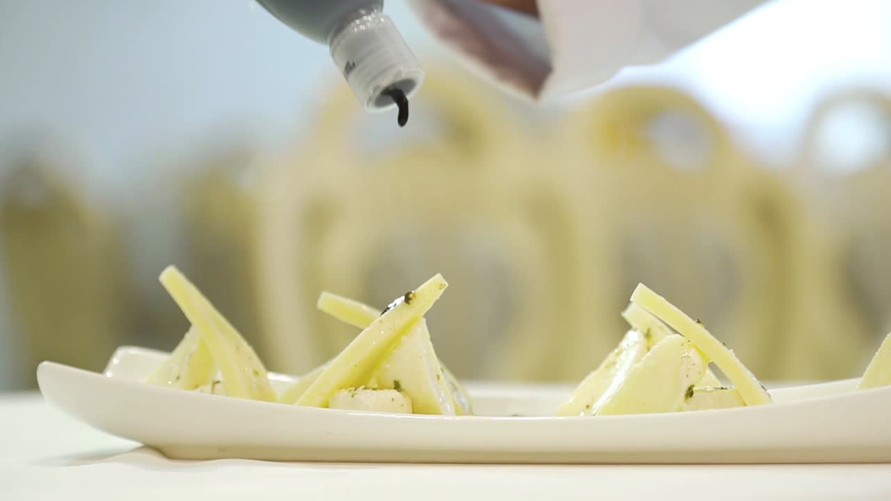 A chef adds delicious sauce to triangular pieces of hard cheese with feta inside on a white plate at a festive table in the restaurant for guests. Close-up.