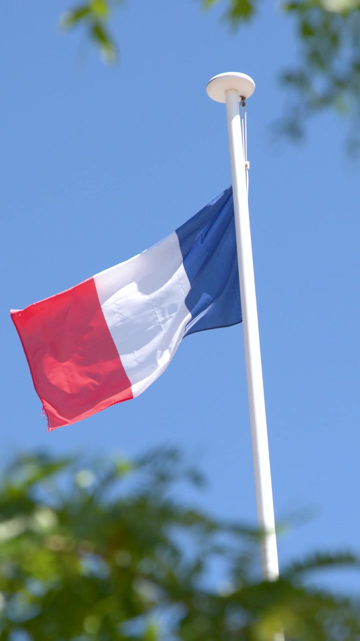 La bandiera nazionale francese sventola da un'asta bianca sotto un cielo estivo limpido e azzurro