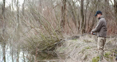 man holding fishing rod walking amidst bare trees 7