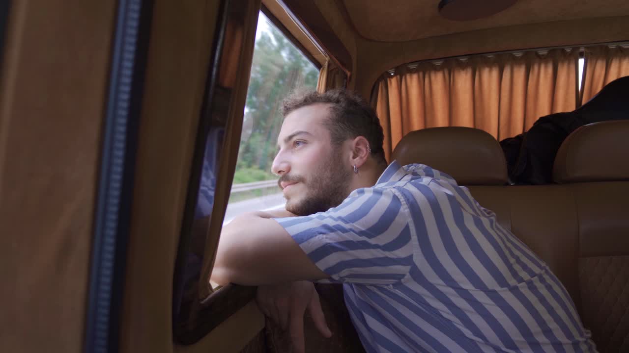 el joven está sentado en el asiento trasero, mirando por la ventana.