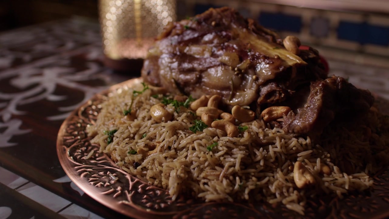 Primer plano de pilaf de cordero y arroz con frutos secos en un plato ornamentado en un entorno tradicional.