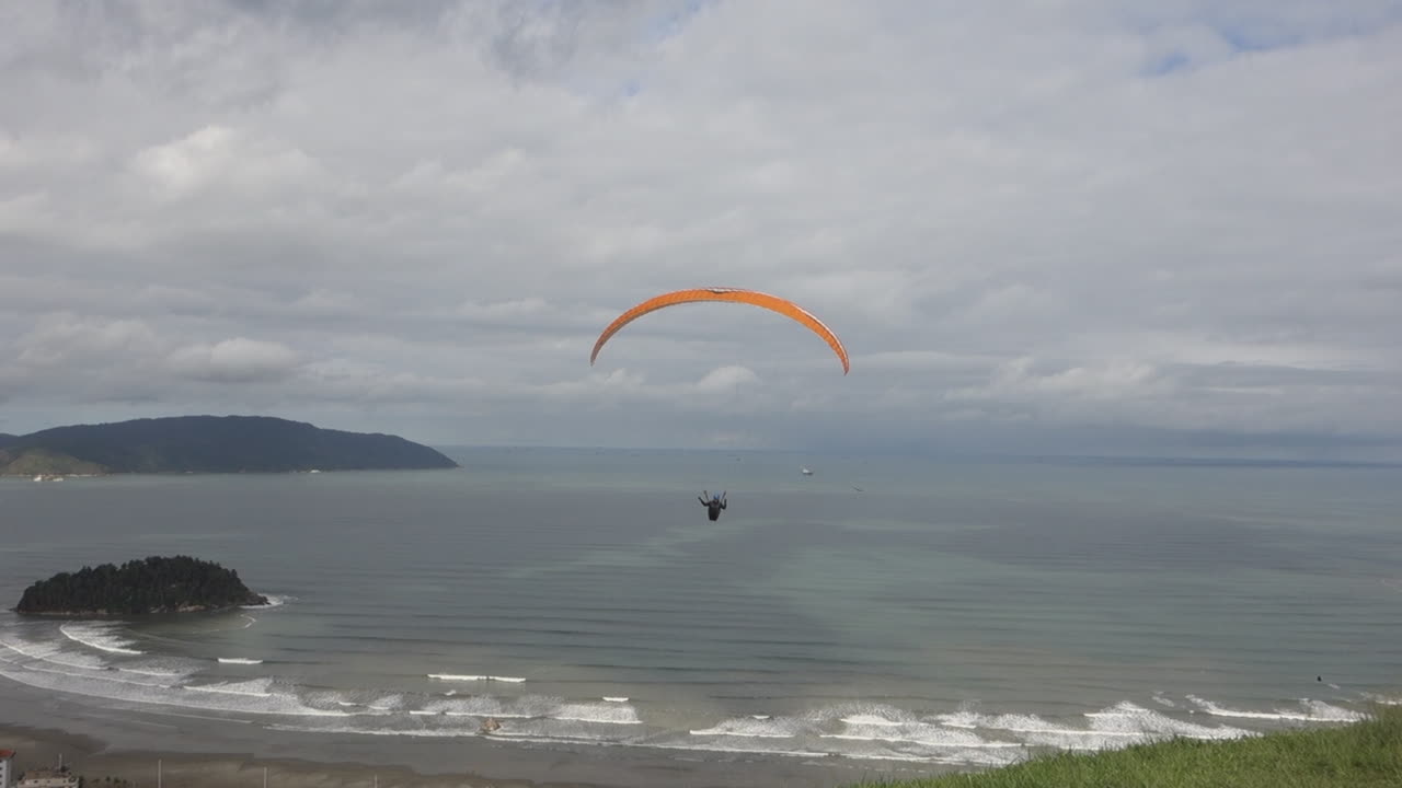 Piloto de parapente despegando desde una rampa de césped muy por encima de una playa nublada