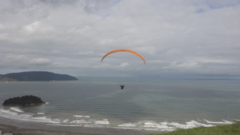 piloto de parapente se lanza desde una rampa de hierba en lo alto de una playa nublada