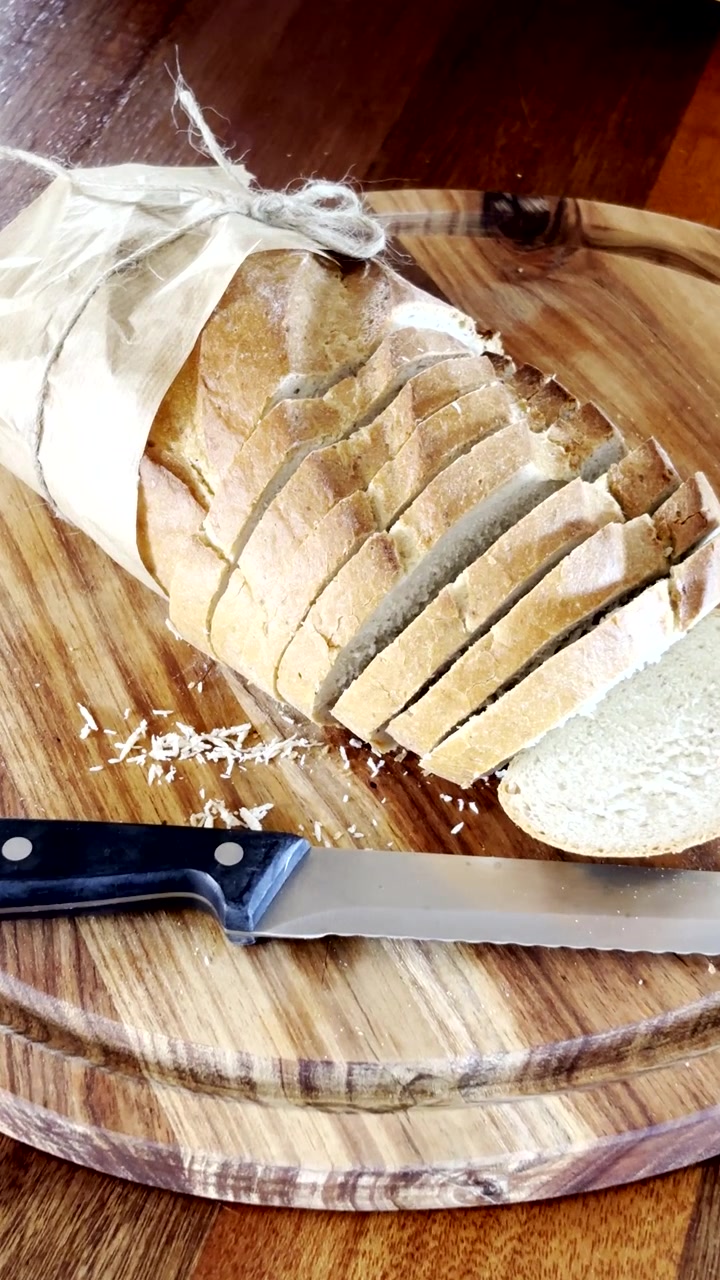 Loaf of bread from bakery cut into slices on wooden cutting board. Vertical