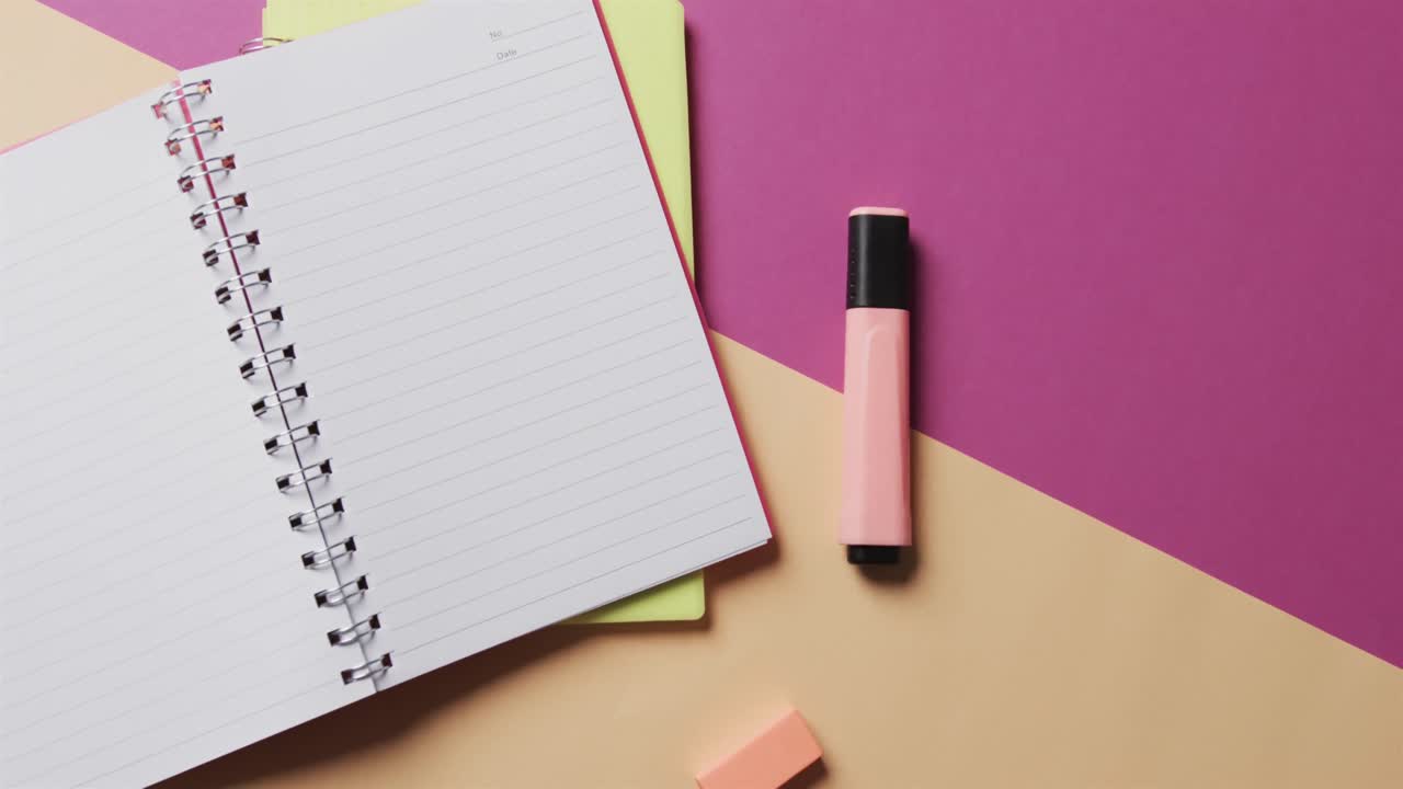 Overhead view of open notebook with school stationery on beige and purple background, in slow motion