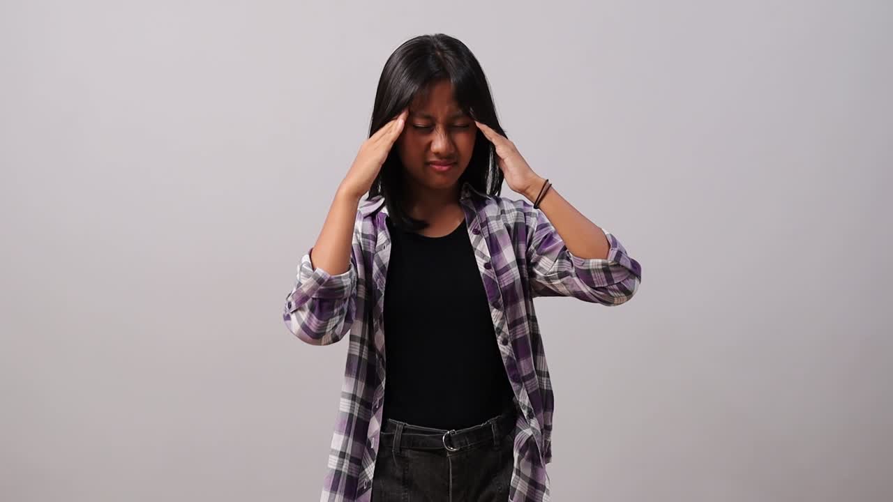 A young asian girl holding their head while showing signs of discomfort