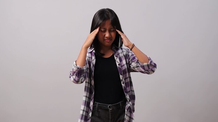 A young asian girl holding their head while showing signs of discomfort