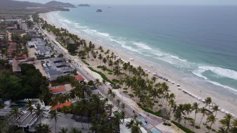 Palm-trees-at-sandy-beach-of-Playa-el-agua-with-driving-motorbikes-on-street