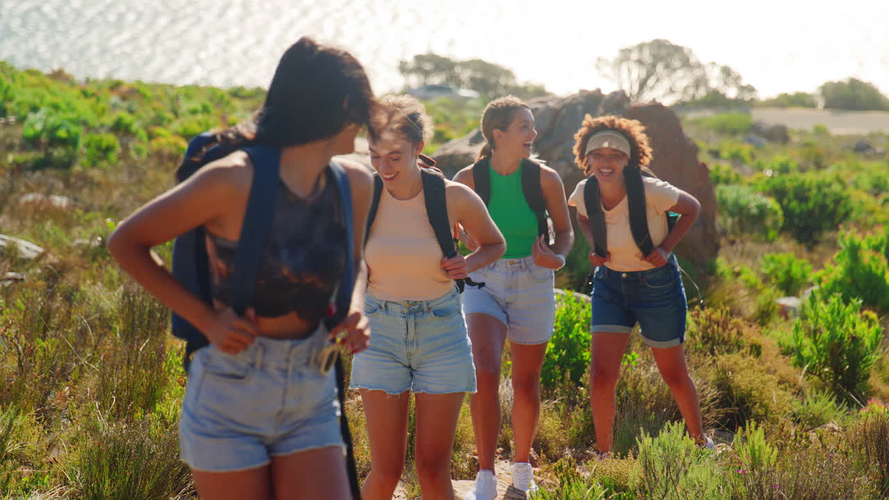 Gruppo di amiche con zaini in vacanza durante un'escursione attraverso la campagna su un sentiero costiero