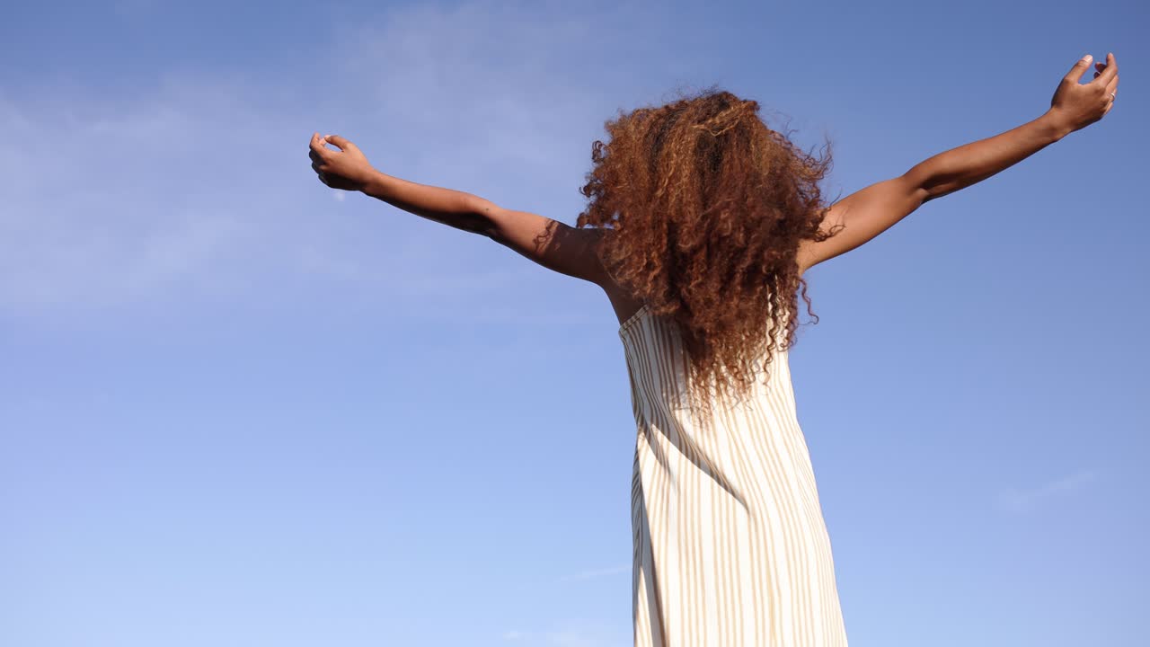 A woman with flowing curly hair expressing freedom and joy under a clear blue sky