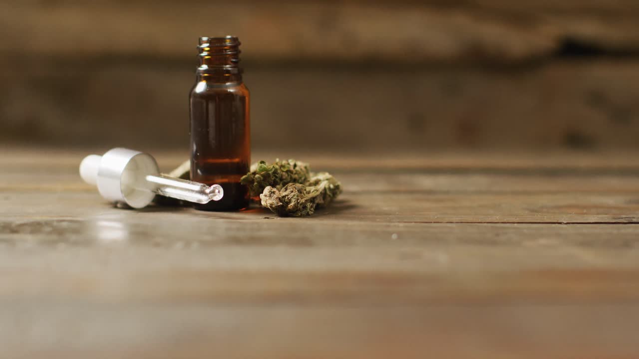 Video di infiorescenze di marijuana e flacone di estratto di CBD su sfondo di legno